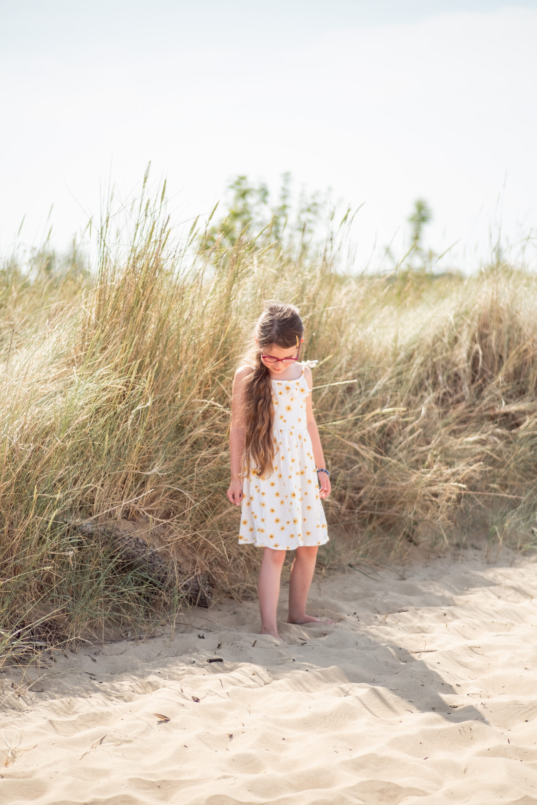 une enfant se tient debout sur le sable à la plage en regardant son ombre